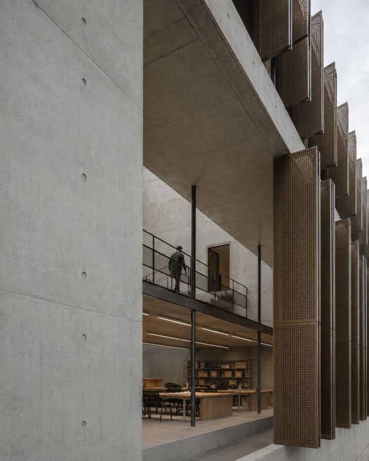 Façade en béton brut à brise-soleil, salle de lecture visible au rez-de-chaussée